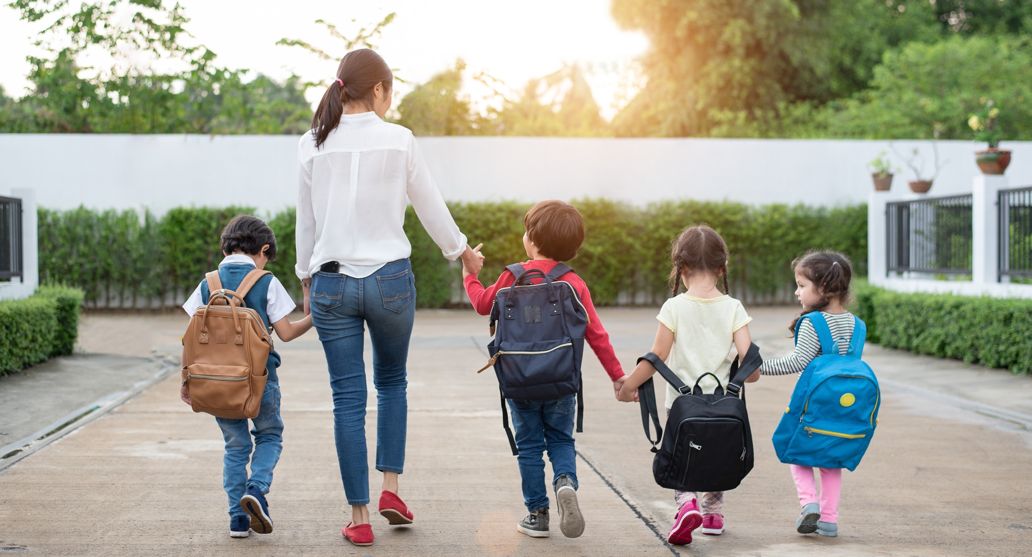 Group of preschool student and teacher holding hands and walking to home. Mom bring her children go to school together. Back to school and Education concept. People and lifestyles theme. Back view